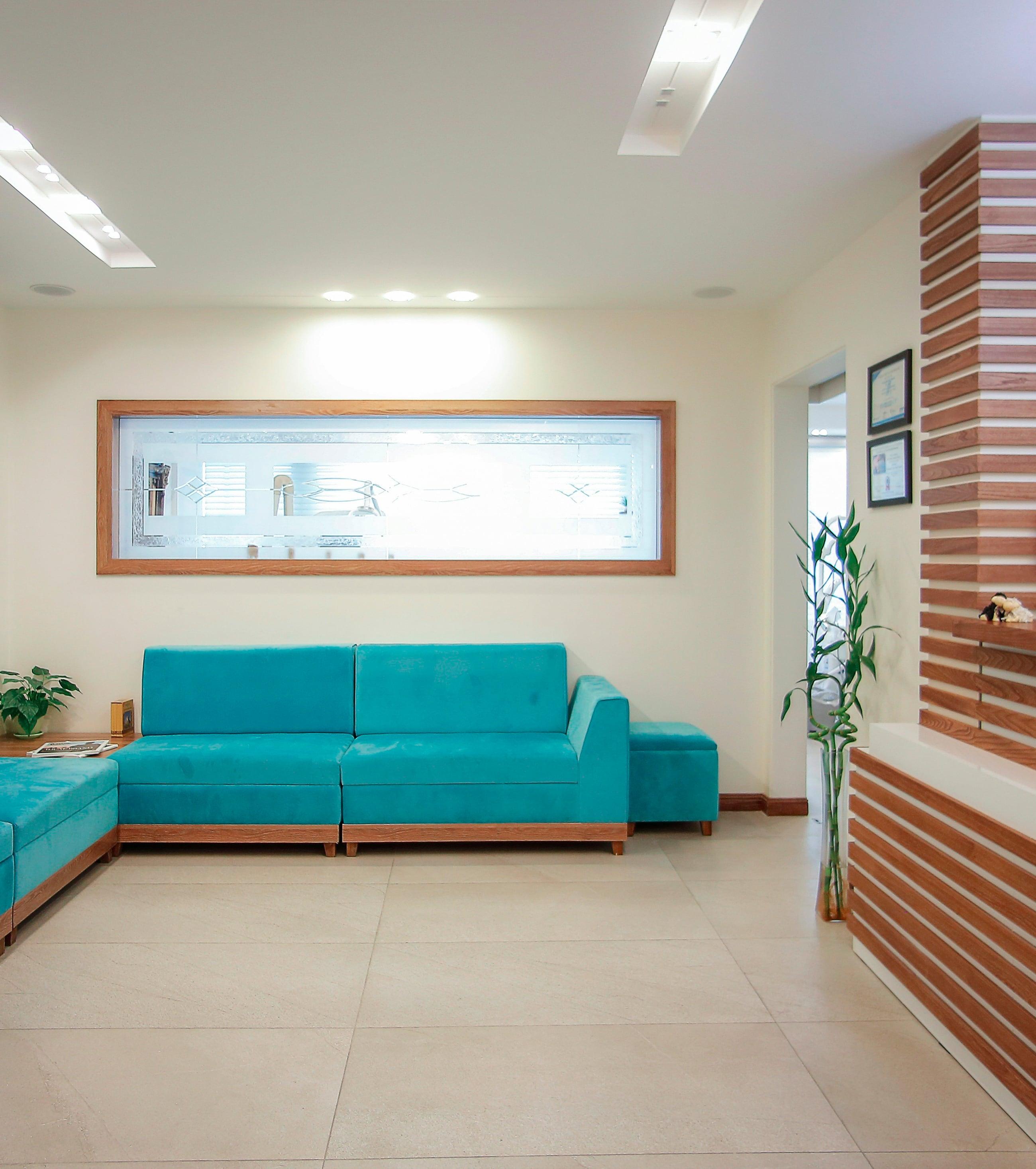 Sala de espera da clínica, com sofás verde-água, piso claro e o balcão de madeira da recepção