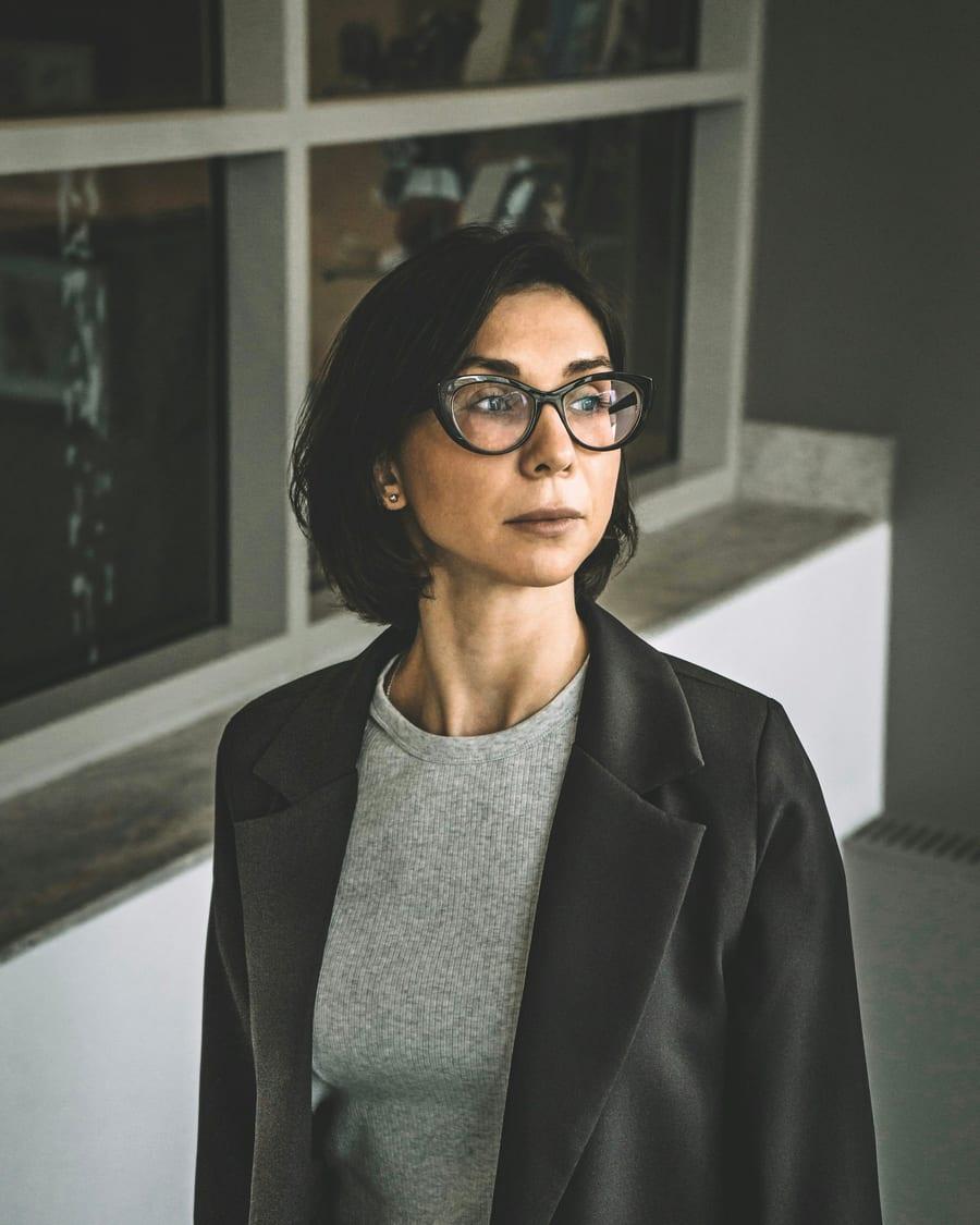 Sandra Lacerda, de óculos e blazer preto, junto à janela do escritório