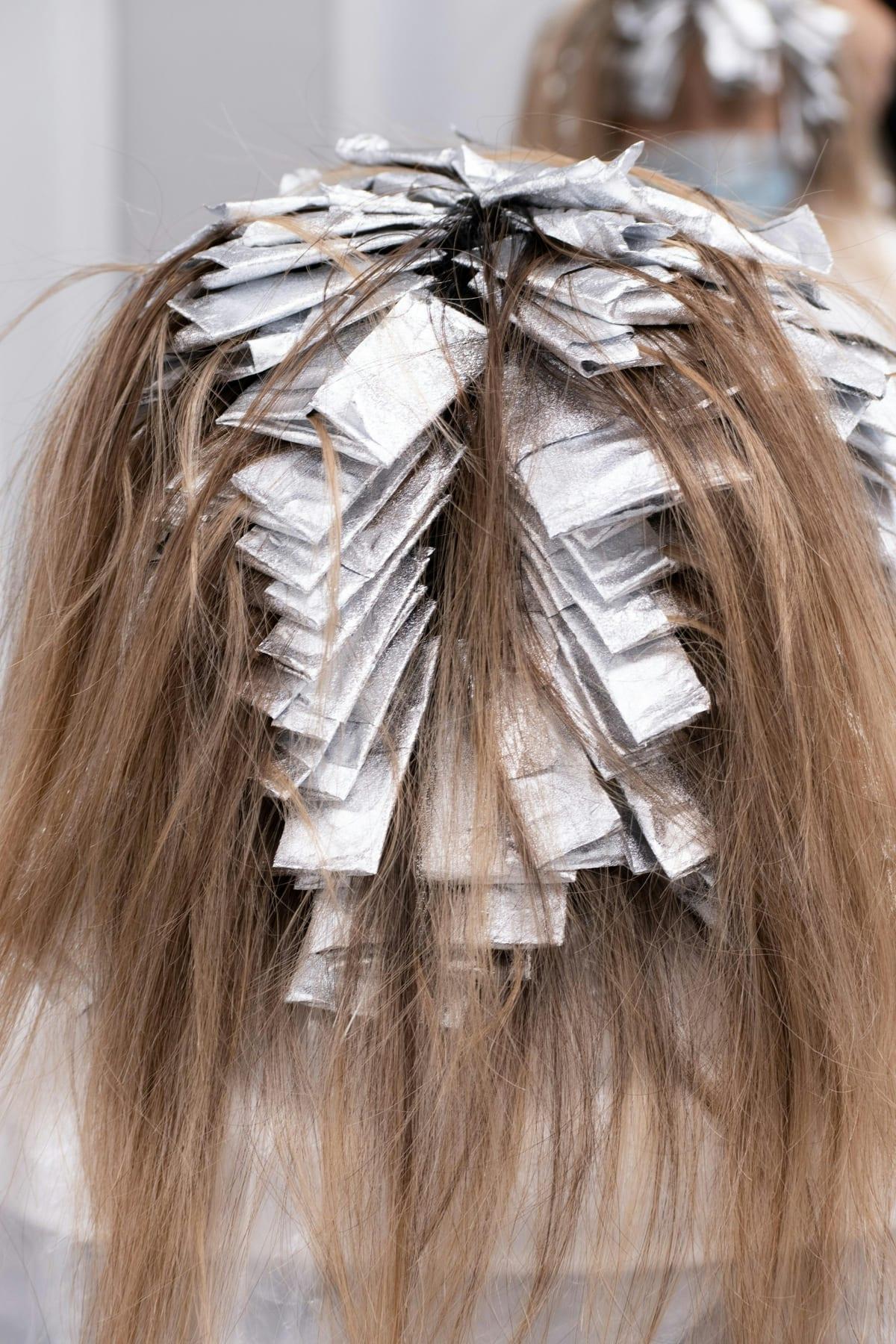 Cabeça de cliente vista de trás, toda dividida em mechas presas em papel alumínio durante o tempo de pausa.