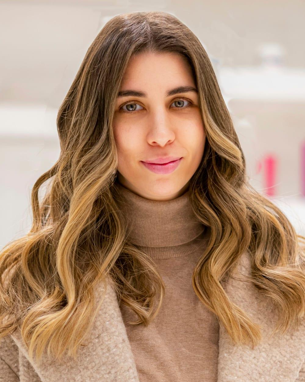 Mulher de cabelo castanho comprido, com mechas loiras do meio às pontas e ondas soltas.