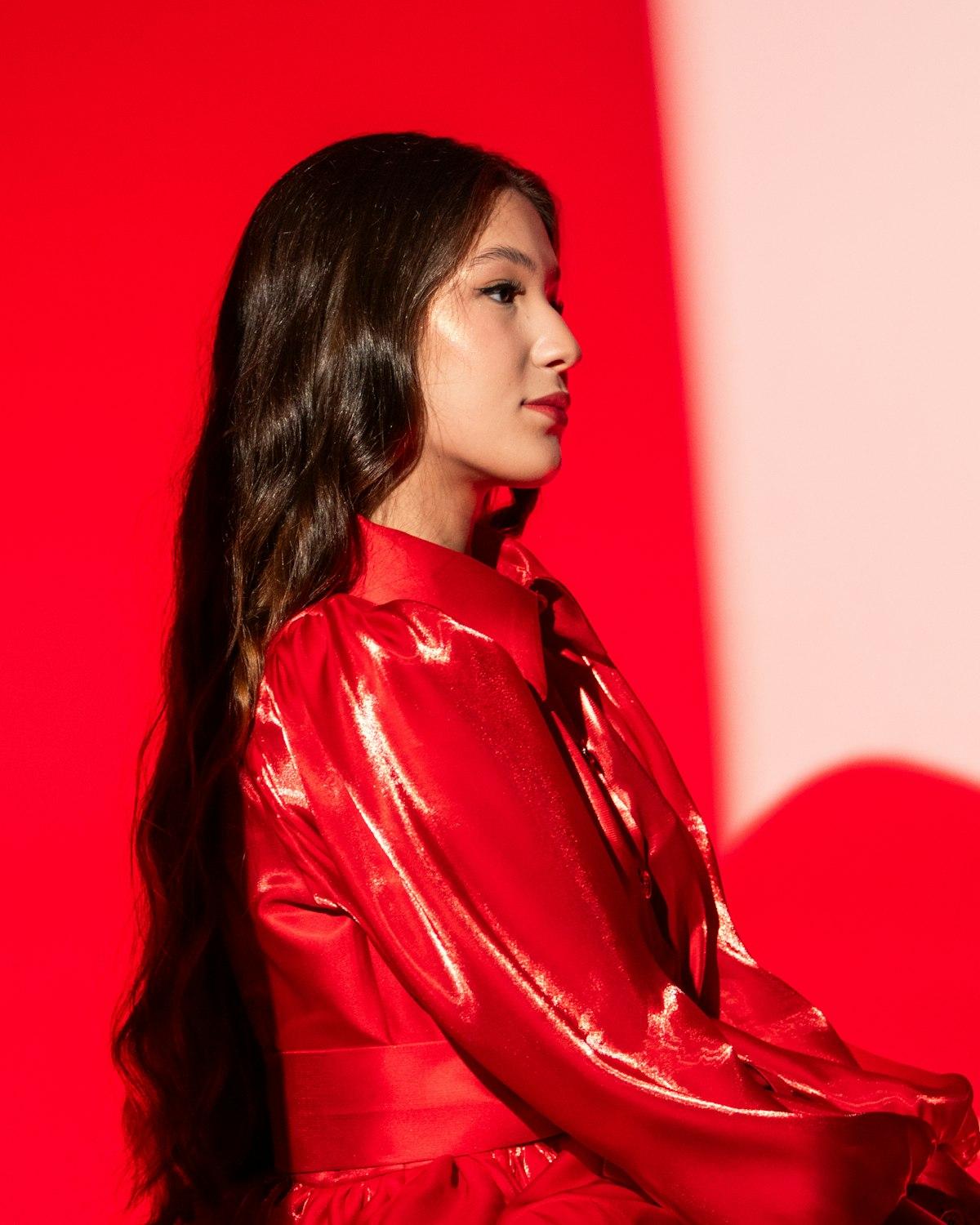 Modelo de perfil com vestido chemise acetinado vermelho de mangas bufantes, em fundo vermelho