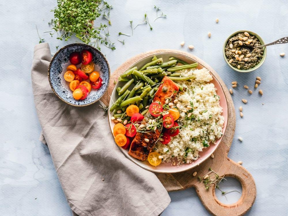 Prato com vagem, tomate, peixe grelhado e cuscuz, com uma tigela de tomatinhos ao lado