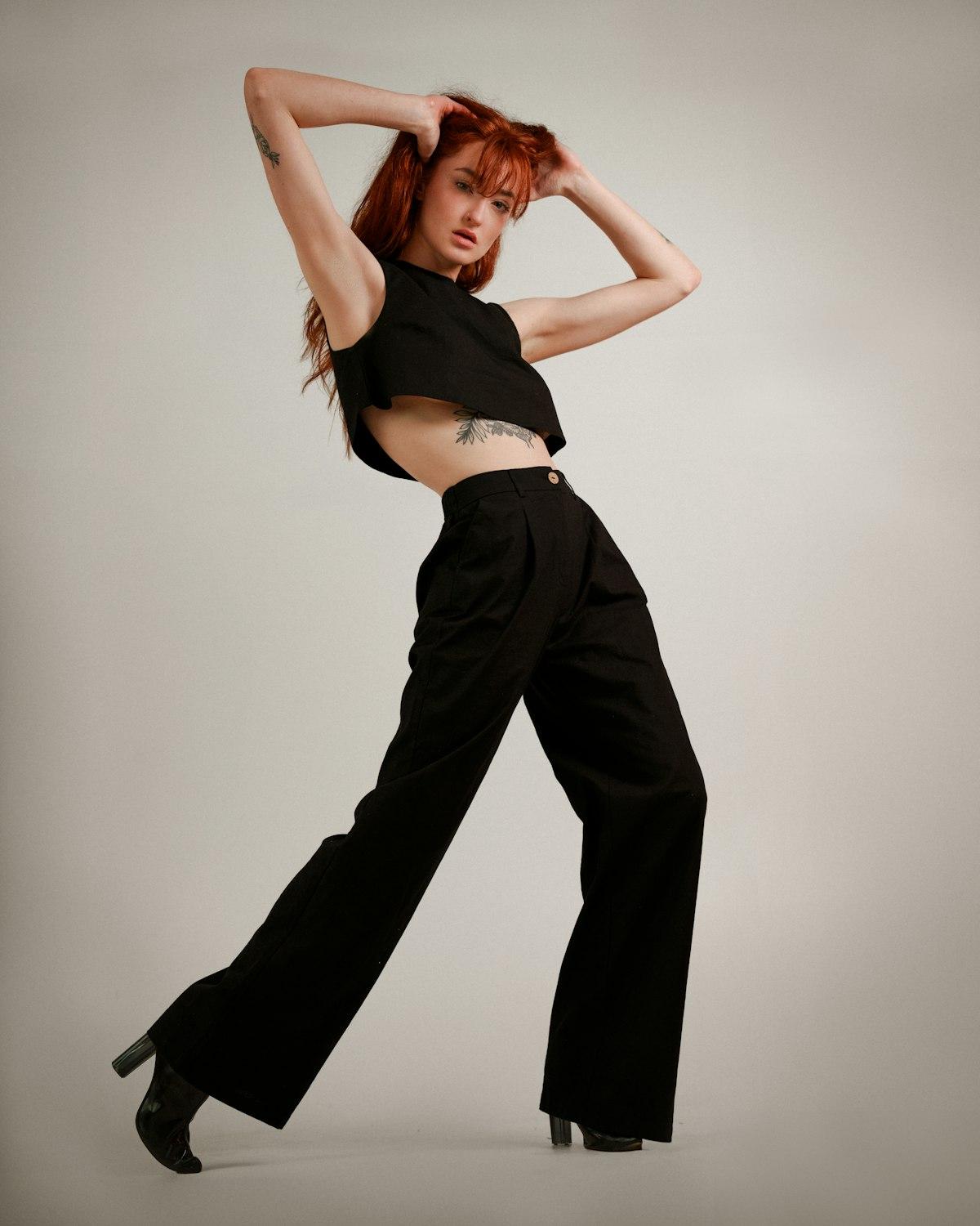 Modelo ruiva em estúdio cinza com blusa cropped preta e calça pantalona preta de cintura alta